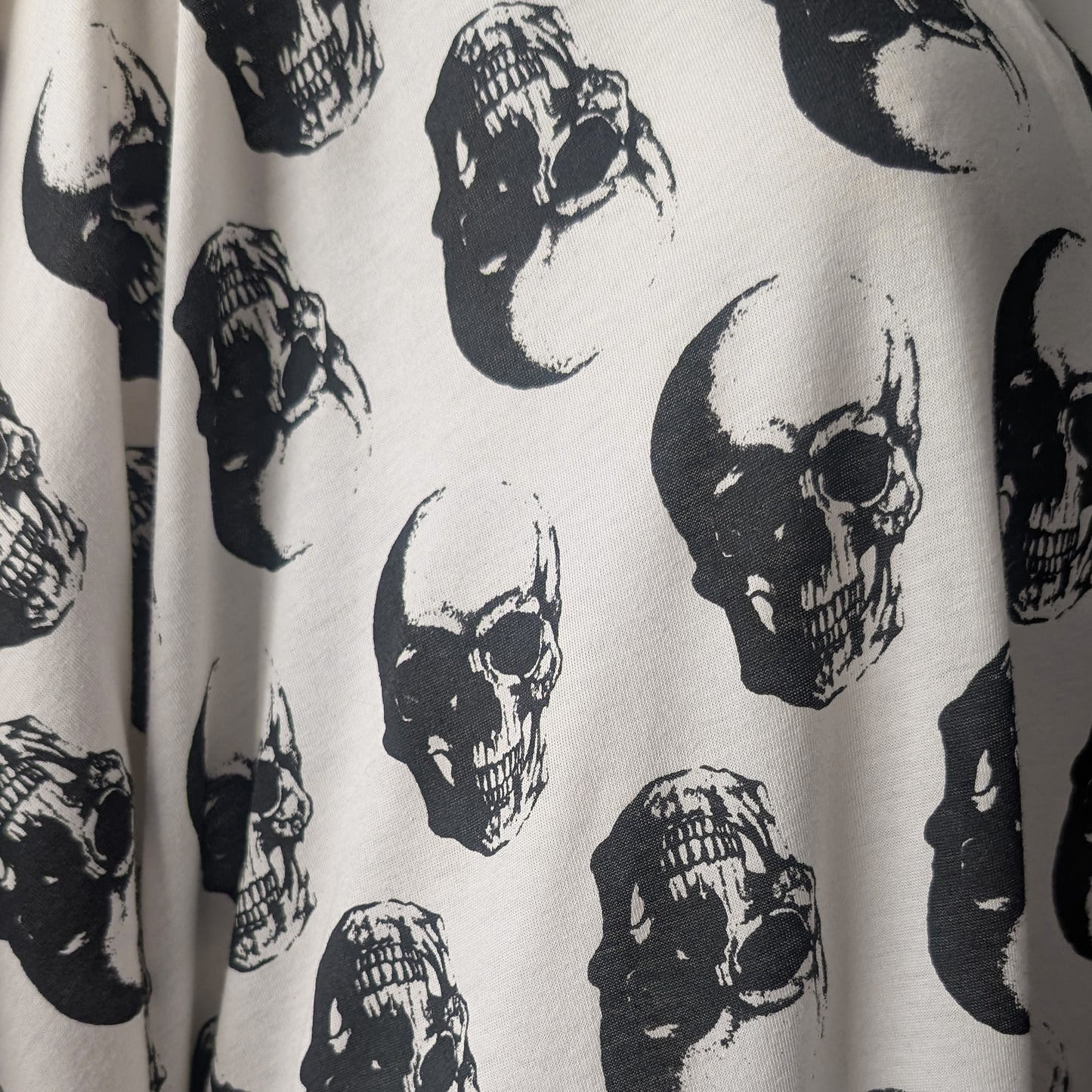 Close-up of a white fabric with an allover black skull print, showing the texture and pattern details.