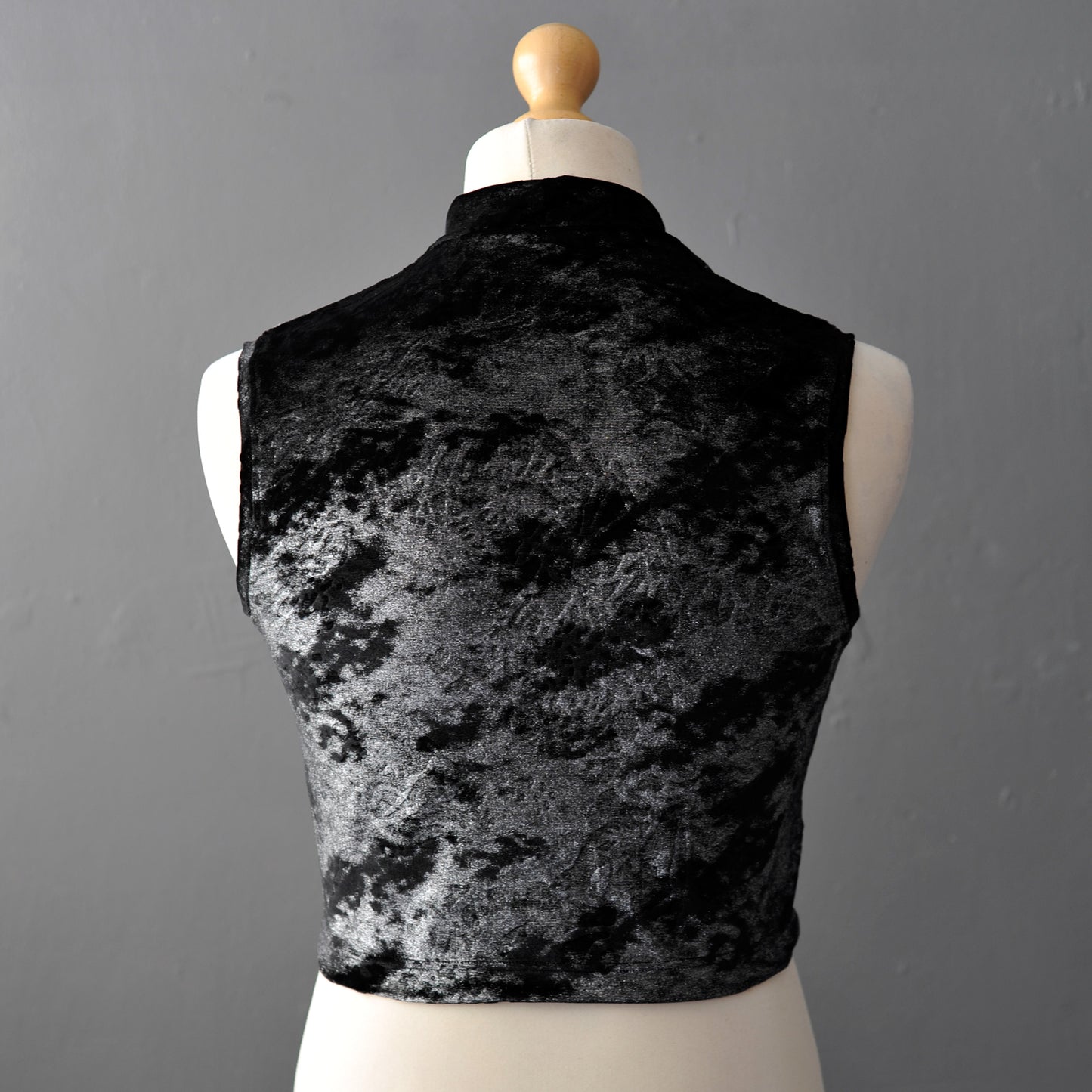 A sleeveless black and silver velvet crop top displayed on a cream dress form mannequin against a gray background.