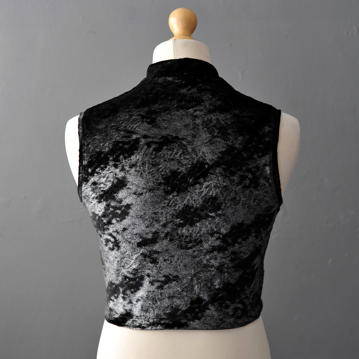 A sleeveless black and silver velvet crop top displayed on a cream dress form mannequin against a gray background.