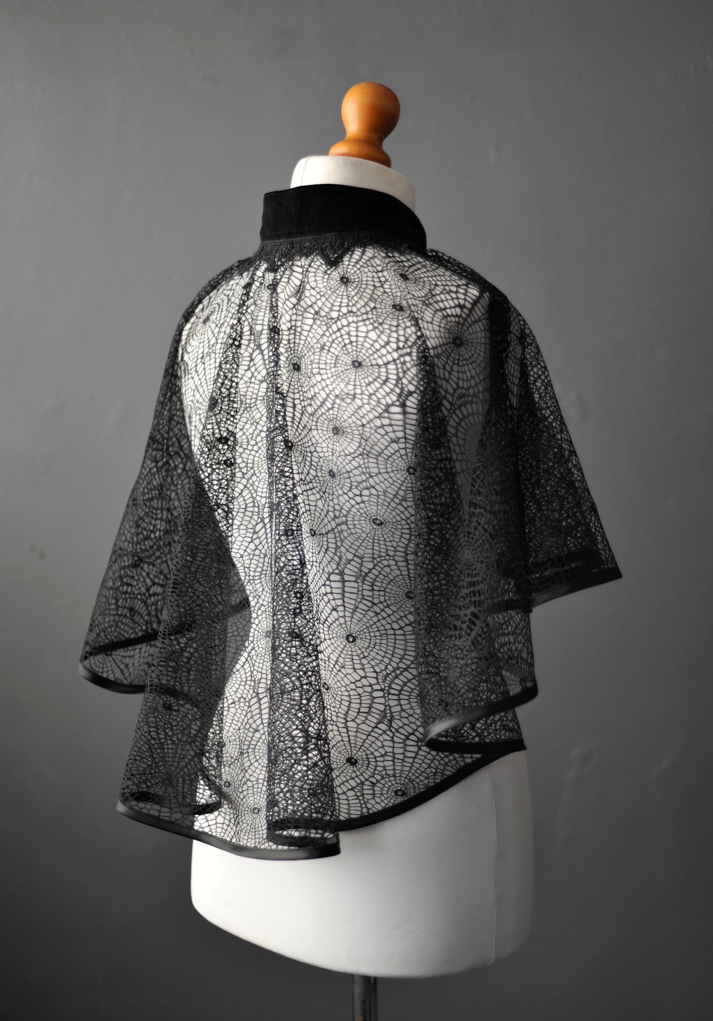 Black lace see through mantle on a mannequin against a gray background