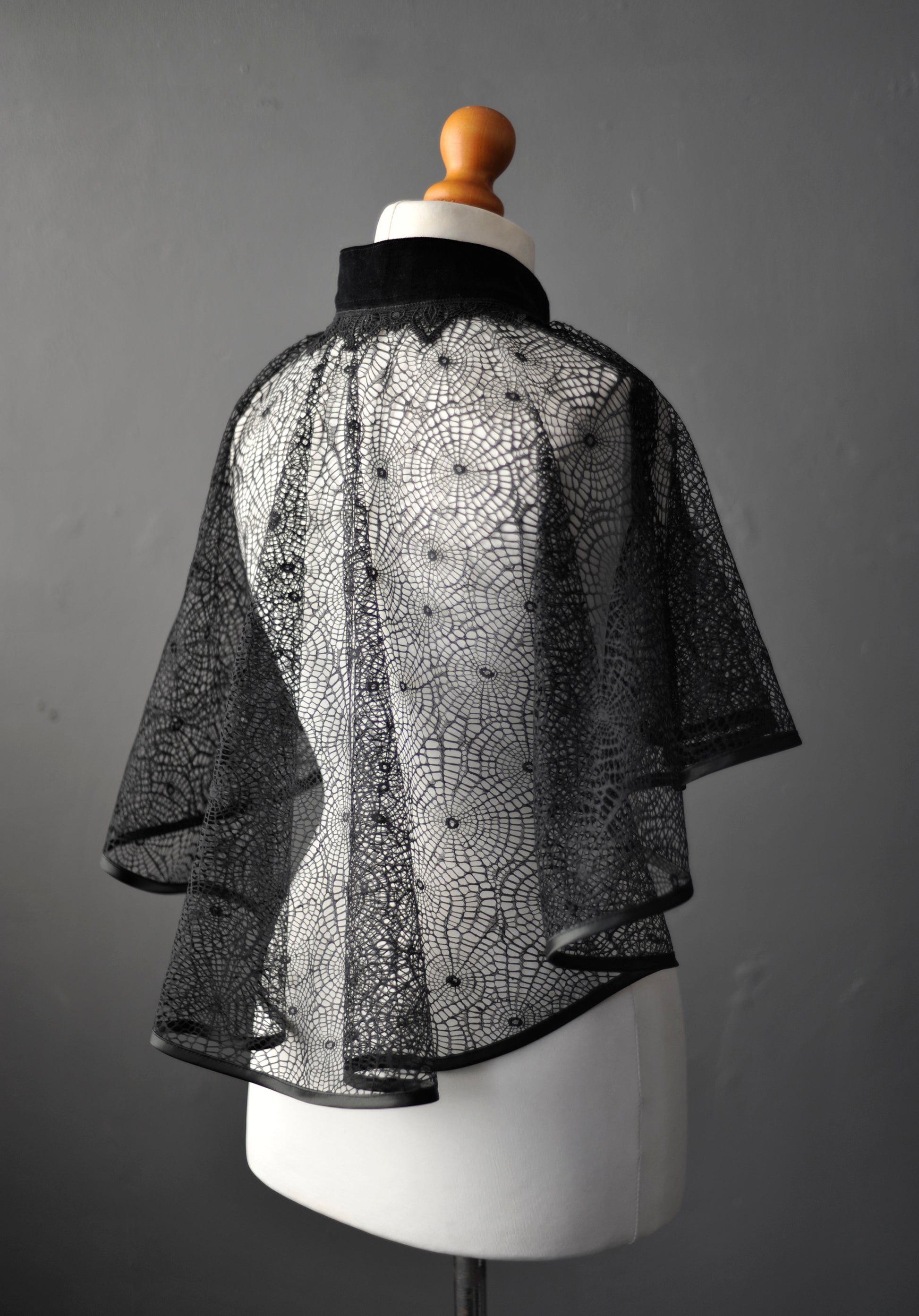 Black lace see through mantle on a mannequin against a gray background