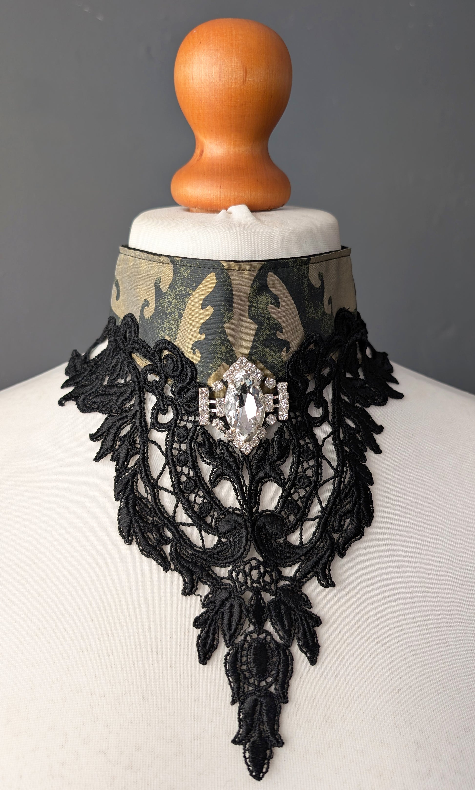 Black lace necklace with a central gemstone on a mannequin against a gray background